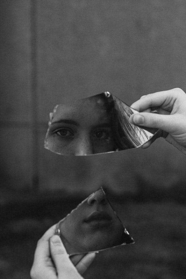 Mujer mirándose en fragmentos de un espejo roto